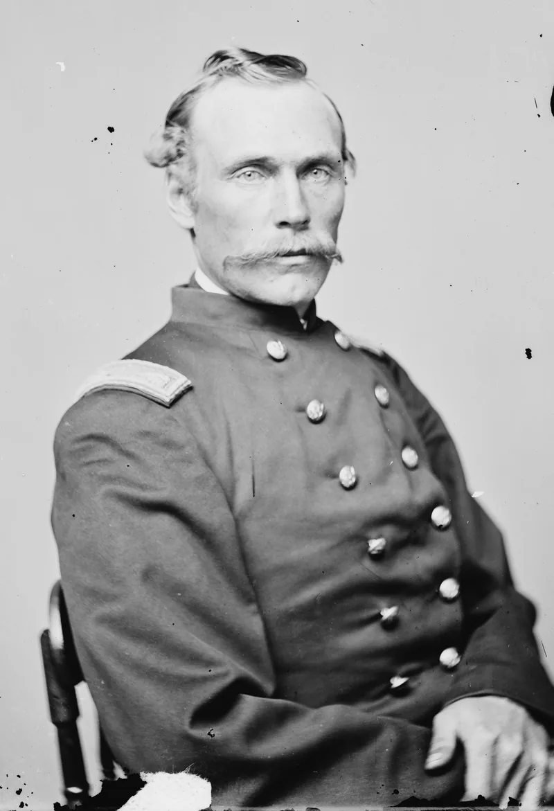 Seated half-length photograph of a Union officer with swept-back hair and a long moustache, in a double-breasted frock coat with shoulder straps.